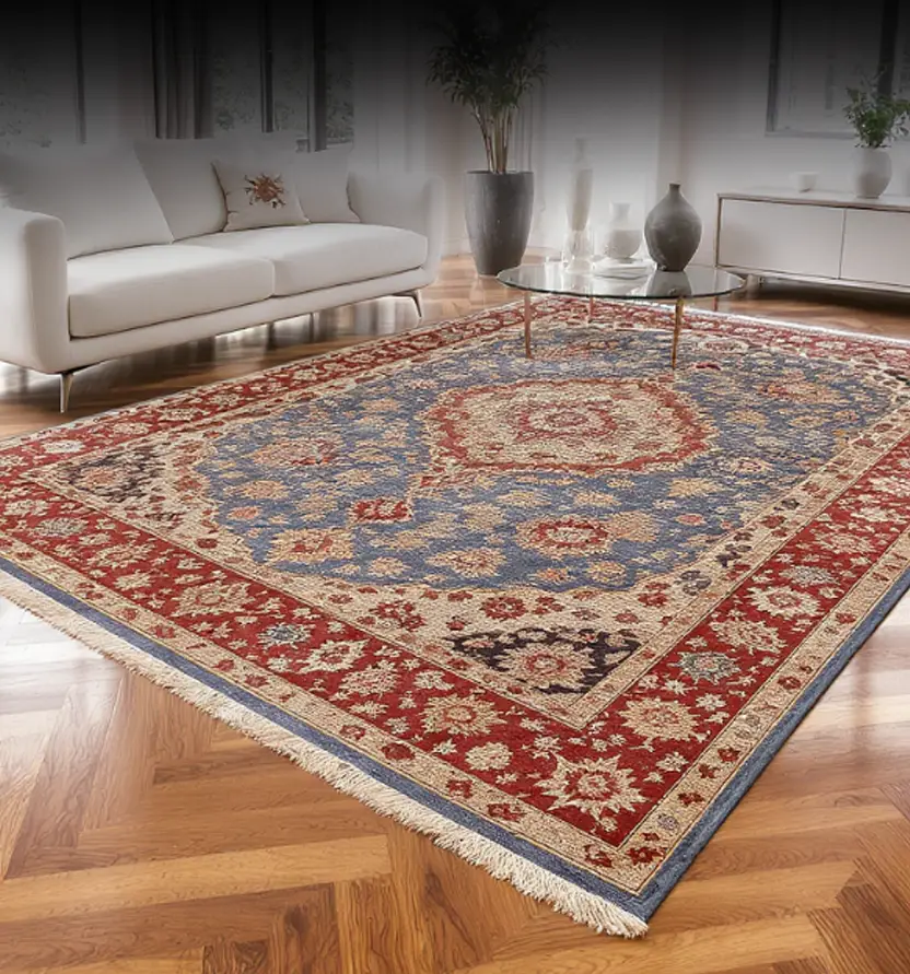 A living room with a patterned area rug featuring red, blue, and beige tones on a herringbone wood floor, with a white sofa and modern decor.