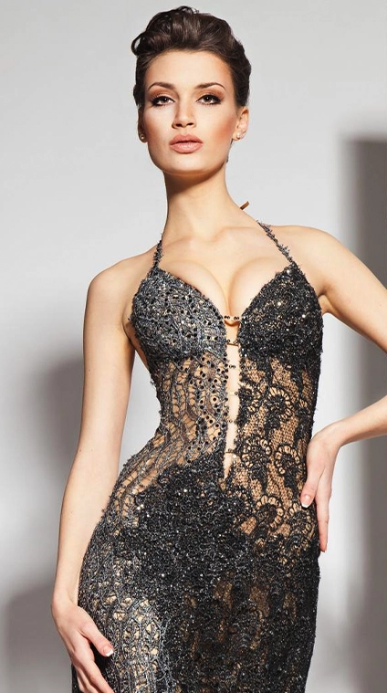A woman poses in a form-fitting, black and silver lace evening gown with a plunging neckline and intricate beadwork.