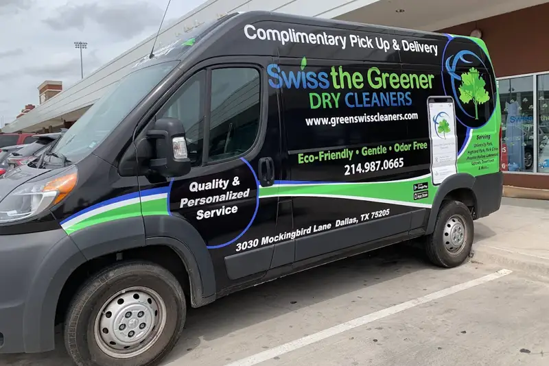 A Swiss the Greener Dry Cleaners van is parked outside a shopping center, promoting eco-friendly and odor-free cleaning with complimentary pick-up and delivery services.