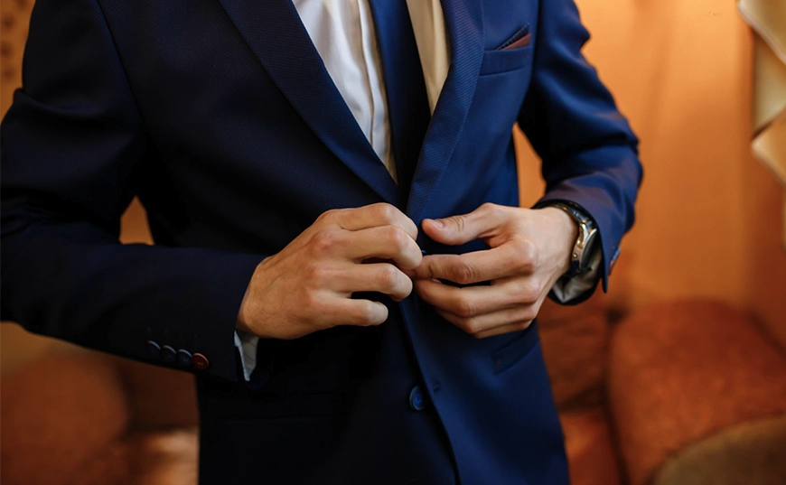 A person in a blue suit and white shirt is buttoning their jacket, with only their torso and hands visible.