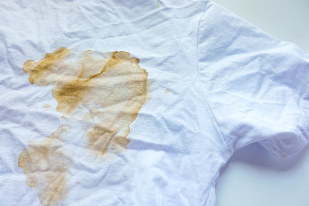 A white t-shirt with a large brown stain on the front, lying on a flat surface.